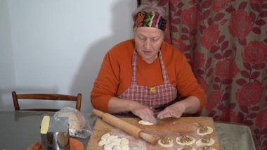 Yaşlı bir kadın etli börek yapar. Ev yapımı hamur. Büyükannem evde yemek pişiriyor. Ellerini mutfak masasına koy..