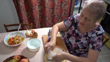 Yaşlı bir kadın mutfakta yemek pişiriyor. Tahta üzerinde balık kesiyor..