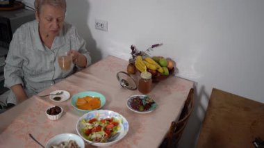 Masada sütlü çay içen yaşlı kadın. Tabakta yemek var. Evde, büyükannenin mutfağında öğle yemeği. Meyve kasesi.