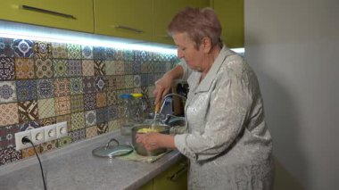 Son sınıf öğrencisi kadın mutfakta öğle yemeği için patates püresi püresi yapıyor. Büyükanne yemek pişiriyor.