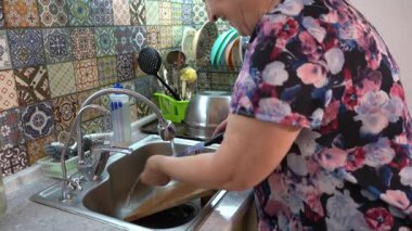 Yaşlı bir kadın mutfak lavabosunda bulaşıkları yıkıyor. Bir bıçak ve tahta kesme tahtası. Büyükannem evde mutfakta yemek pişiriyor.