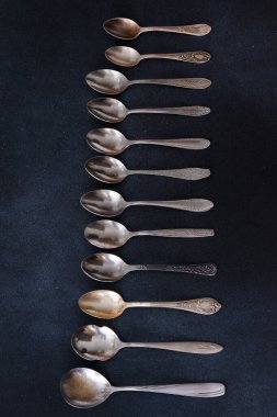 Farklı kaşıklar. Siyah arka planda gümüş çatal bıçak seti. Kaşığı masaya koy. Eski çatal bıçak takımı
