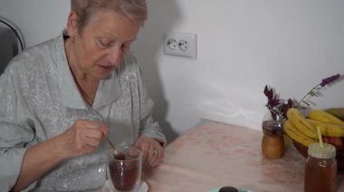 Çay kaşığıyla çay poşetini karıştır. Masada çay içen yaşlı kadın. Tabakta yemek var. Evde, büyükannenin mutfağında öğle yemeği. Kahvaltı.