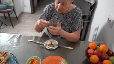 Yaşlı bir kadın kahvaltı yapıyor. Büyükannem evde masada mutfakta otururken kahve içiyor ve süzme peynir güveci yiyor. Çatal ve bıçak. Değişken odak