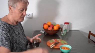 Kahvaltıdan sonra kahve içen yaşlı bir kadın. Fincanda çay kaşığıyla karıştırmak. Boş tabakları masaya koy. Meyve kasesi yemeği..