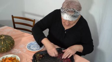 Yaşlı bir kadın kurutulmuş böğürtlen hasadını sınıflandırıyor. Bir büyükanne mutfaktaki masada yemek hazırlar. Ev yemeği. Tabak masasında kuru meyve.