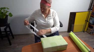 Beyaz bir kurdele bağla. Yaşlı bir kadın hediyesini yeşil kağıda sarar. Bir büyükanne evde bir kutu toplar. Eller yukarı görünüm