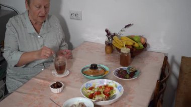 Çay kaşığıyla çay poşetini karıştır. Yaşlı kadın masada çay içer. Tabakta yemek var. Evde, büyükannenin mutfağında öğle yemeği. Kahvaltı.