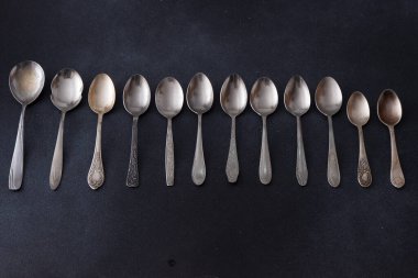 Farklı kaşıklar. Siyah arka planda gümüş çatal bıçak seti. Kaşığı masaya koy. Eski mutfak eşyaları.