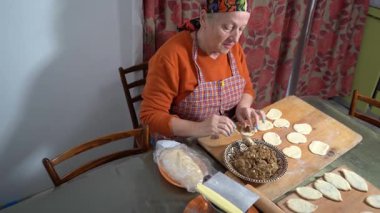 Yaşlı bir kadın etli börek yapar. Ev yapımı hamur. Büyükannem evde yemek pişiriyor.