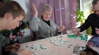Yaşlı kadın bingo oynuyor. Ailesi olan bir büyükanne birlikte vakit geçirir. Evde masa oyunu. Lotto masada. Mutlu insanlar.