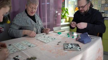 Yaşlı bir kadın emekli bingo oynuyor. Mutlu ailesiyle evde masa oyunu oynayan bir büyükanne. Lotto masada. Birlikte iyi vakit geçirdik..