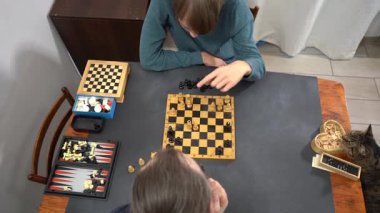 Satranç tahtası ve satranç taşları. Genç çocuk evde baba ve kediyle masa oyunu oynuyor. Ailecek vakit geçireceğiz. Tablo üstü görünümü