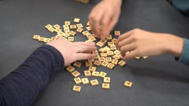 Scrabble oyunu. Oyuncuların elleri harf dizer. Tablo üstü görünümü