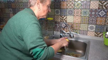 Yaşlı bir kadın mutfak lavabosunda patates soyuyor. Evde sebze pişir. Büyükanne yemek yapıyor.