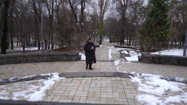 Yaşlı kadın parkta basamakları tırmanır. Bir büyükanne kışın yürür. Soğuk ve açık havada kar