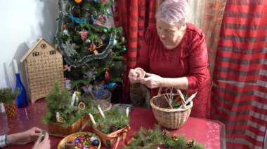 Büyükannem Noel çelengi süslemesi yapar. Yaşlı kadın kendi elleriyle dekore ediyor. Büyükanne evde mutlu bir şekilde gülümsüyor. Kırmızı elbise. Zanaat