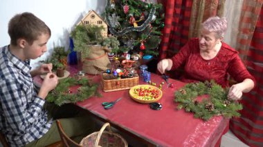 Büyükannem ve torunum birlikte Noel ağacı çelengi yapıyorlar. Yaşlı kadın ve genç çocuk kendi elleriyle dekore ederler. Aile eğlencesi. Zanaat