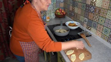 Bir kadın turta pişiriyor. Evde kızarmış yemek pişirmek. Büyükanne mutfak ocağında yemek pişiriyor.