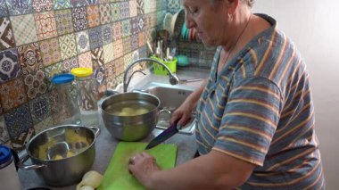 Yaşlı bir kadın yemek pişiriyor. Mutfak yüzeyinde patates doğrama. Büyükanne yemek pişirir Sebze keser