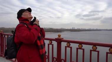 Yaşlı kadın nehrin üzerindeki bir köprüde duruyor. Bir büyükanne soğuk havada dışarıda yürür. O bir şapka ve ceket giyiyor. Açık hava.