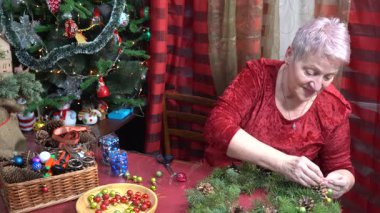 Büyükannem Noel çelengi yapıyor. Yaşlı kadın çam dallarını süslüyor. Kış el yapımı. Tatil hobisi. Son sınıf aktiviteleri