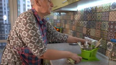 Yaşlı kadın çatal ve kaşıkları ayırıyor, yıkadıktan sonra bulaşıkları yıkıyor. Mutfak gereçlerini çekmeceye koyuyorum. Önlüklü büyükanne. Mutfak evi.