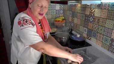 Yaşlı bir kadın hamur tatlısı yapar ve pişirir. Ukrayna yemeği. Nakışlı gömlekli büyükanne. Ocakta bir tencere kaynıyor. Mutfak evde..