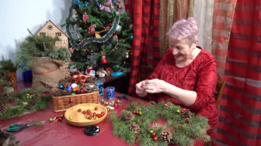 Büyükannem Noel çelengi yapıyor. Yaşlı kadın gülümsüyor ve eğleniyor. Kış el yapımı. Ladin dalları