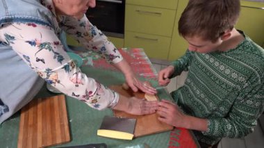 Büyükannem torununa hamurdan kurabiye yapmayı öğretiyor. Evde yemek pişir. Masada pişirme. Eller yukarı. Tahta tahta. Yaşlı kadın ve genç çocuk mutfakta birlikte yemek pişiriyorlar..