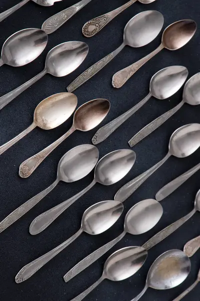 Farklı kaşıklar. Siyah arka planda gümüş çatal bıçak seti. Kaşığı masaya koy. Eski mutfak eşyaları.