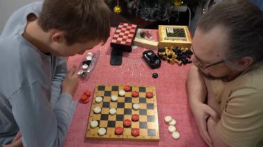 Genç bir çocuk babasıyla dama oynuyor. Satranç tahtası. Masanın üstünde masa oyunu var. Birlikte oynayın