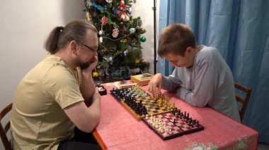 Baba ve oğul aynı anda üç tahtada satranç oynarlar. Genç çocuk tek seferlik bir oyun oynuyor. Aile Noel 'i birlikte