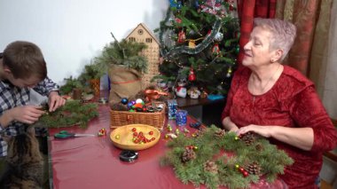 Büyükannem ve torunum birlikte Noel çelengi yapıyorlar. Yaşlı kadın ve genç çocuk kendi elleriyle dekore ederler. - Aile. Zanaat. Kedi