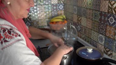 Kaynar suda hamur köftesi pişirmek. Yaşlı bir kadın ocakta yemek pişiriyor. Varenyky 'yi bir tencereye koymak.