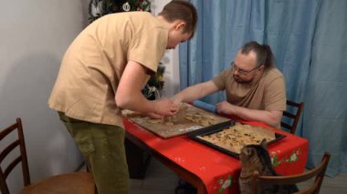 Bir adam ve bir genç çocuk hamurdan kurabiye kesiyorlar. Baba ve oğul birlikte yemek pişiriyorlar. Baba aşçı. Evde kedi var. Noel pastaları