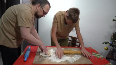 Diz çök ve hamuru merdaneyle yuvarla. Ve genç bir çocuk hamurdan kurabiye kesiyor. Baba ve oğul birlikte yemek pişiriyorlar. Baba aşçı. Evde kedi var. Noel
