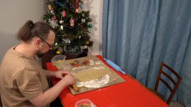 Adam hamuru ahşap bir tahtada merdaneyle yuvarlıyor. Pasta ve kurabiye pişiriyorum. Noel yemeği pişirmek. Tablo