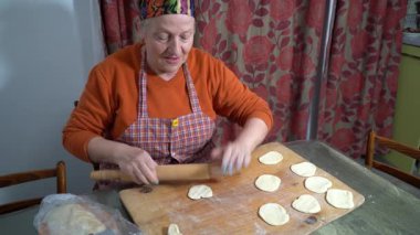 Büyükanne hamuru tahta bir oklavayla yuvarlıyor. Kadın evde masada turta pişiriyor. Yemek pişirmek..