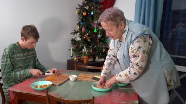 Çocuk kurutulmuş kayısıları bıçakla keser. Yaşlı kadın hamur yoğuruyor. Büyükannesi ve genç torunu kışın evde Noel kurabiyesi pişirmeye hazırlanıyorlar. Mutfakta bir Noel ağacı. Yemek masası