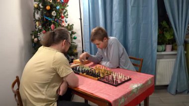 Baba ve oğul aynı anda üç tahtada satranç oynarlar. Genç çocuk babasıyla oyun oynuyor. Evde ailecek vakit geçiririz..