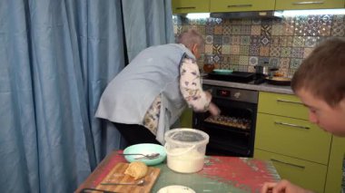 Yaşlı bir kadın kurabiyeleri fırından çıkarır. Ev yapımı pişirme. Yemek pişirmek. Büyükanne ve torun yemek hazırlıyor..