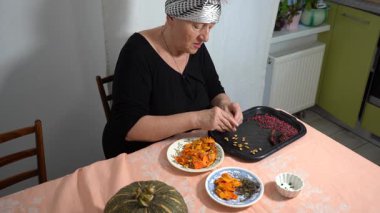 Kurutmak için kabak çekirdeği topluyorum. Yaşlı bir kadın böğürtlen tohumlarını kurutuyor. Mutfak masasında bir büyükanne oturuyor. Yemek pişirme