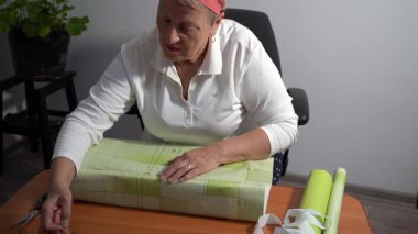 Yeşil ambalaj kağıdına bantla yaşlı bir kadın hediyesini yeşil kağıda sarar. Bir büyükanne evde bir kutu toplar. Eller yukarı görünüm