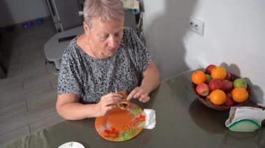 Yaşlı bir kadın kahvaltıda turta yer. Büyükanne yemekten hoşlanır. Yemek portakal tabağı. Tablo