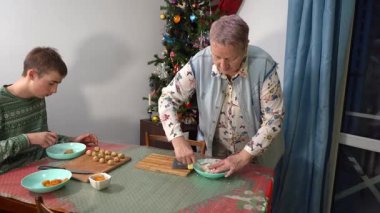 Meyveli turta yapıyorum. Bir çocuk ve büyükannesi noel pastası hamuru pişiriyor. Yaşlı bir kadın ve genç bir kız mutfak masasında yemek pişiriyorlar. Kurabiyeler pişer.