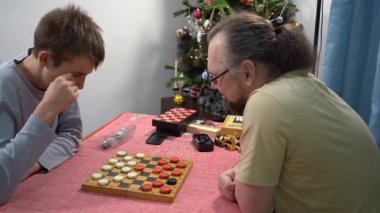 Ergen, babasıyla dama oynuyor. Satranç tahtası. Oğlan ve babası evde masa oyunu oynuyorlar.