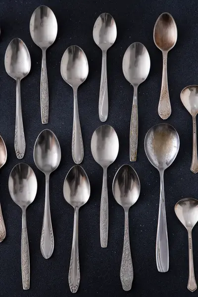 Farklı kaşıklar. Siyah arka planda gümüş çatal bıçak seti. Sofra sofrasında kaşık.
