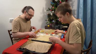 Kedi yemek tepsisinden kurabiye çalar. Erkek ve genç bir çocuk hamurdan kurabiye yapıyor. Baba ve oğul birlikte yemek pişiriyorlar. Babam evde yemek yapıyor.