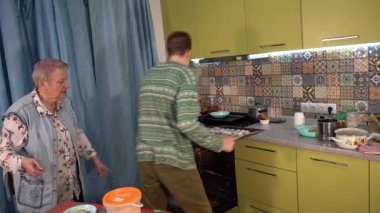 Çocuk fırına kurabiye tepsisi koyar. Bir genç, evdeki mutfakta büyükannesiyle yemek pişirir. Pişirme ve pişirme